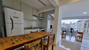 Una cocina moderna con una gran mesa de madera y sillas, un refrigerador y vistas de la ciudad a través de amplias ventanas.