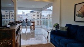 Una sala de estar moderna con un sofá azul, un comedor con mesa y sillas, y un balcón con vista a otros edificios.