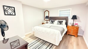 A bedroom with a bed, bedside tables, a mirror, a fan, and a dresser. - 1BR Private Suite · West Vancouver · Landmark View · Prime Location (West Vancouver)