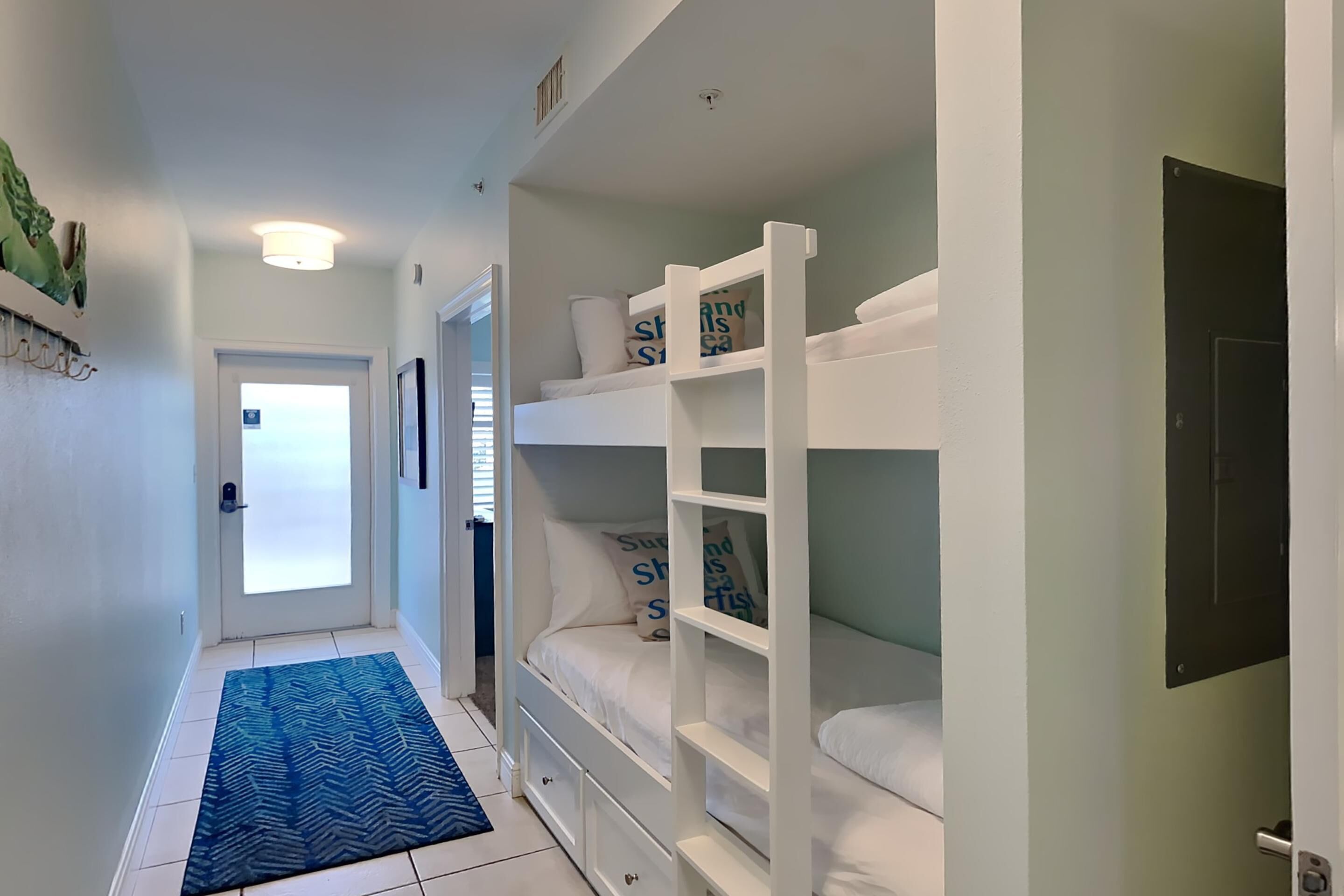A hallway with a bunk bed, a blue patterned rug, and a door leading to another room.