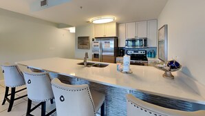 A modern kitchen with a large island, bar stools, stainless steel appliances, and a decorative bowl on the counter. - Cassine Station #305 by Southern Vacation Rentals (Santa Rosa Beach)