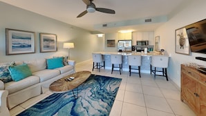 A modern living room with a sofa, coffee table, and a kitchen area in the background. - Cassine Station #305 by Southern Vacation Rentals (Santa Rosa Beach)