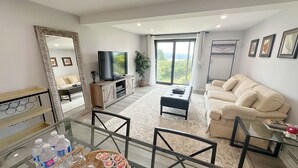 A modern living room with a sofa, TV, and a dining area with a glass table. - 2BR Private Suite · West Vancouver · Landmark View · Prime Location (West Vancouver)