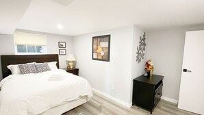 A neatly arranged bedroom with a bed, bedside table, lamp, and a small cabinet. - 2BR Private Suite · West Vancouver · Landmark View · Prime Location (West Vancouver)