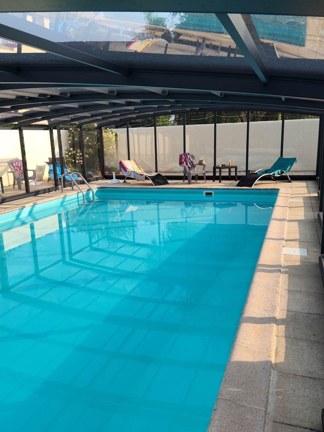 Una piscina interior con agua cristalina, rodeada de sillones de descanso y un área de estar cubierta.