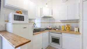 Una cucina compatta con mobili bianchi, un forno a microonde, una lavastoviglie, un forno e un piano di lavoro in legno.