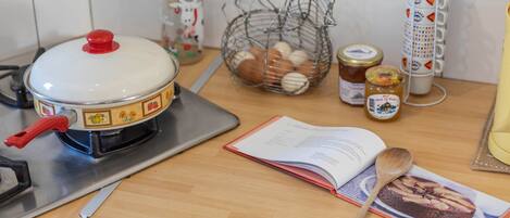 A kitchen counter with a stove, a cookbook, a wooden spoon, a jar of jam, and a basket of eggs.