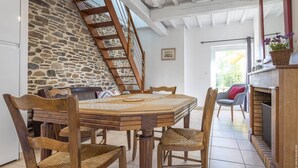 Zona pranzo con parete in pietra, tavolo e sedie in legno. Una scala in legno conduce a una soffitta.