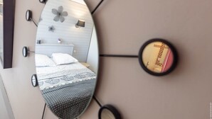 A bedroom with a bed, a nightstand, a mirror, and a wall-mounted light fixture. - Cottage Kerruer (CHERRUEIX)