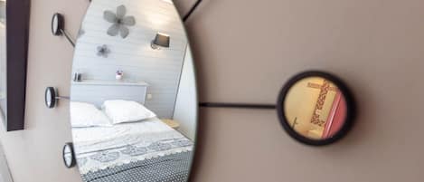 A bedroom with a bed, a nightstand, a mirror, and a wall-mounted light fixture.