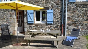 A stone building with a wooden picnic table, a yellow umbrella, and a lounge chair. - Cottage Kerruer (CHERRUEIX)