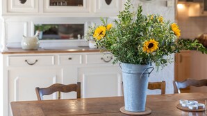 A dining table with a metal bucket of flowers, white cabinets, and a clock on the wall. - Cottage Roazhon (CHERRUEIX)