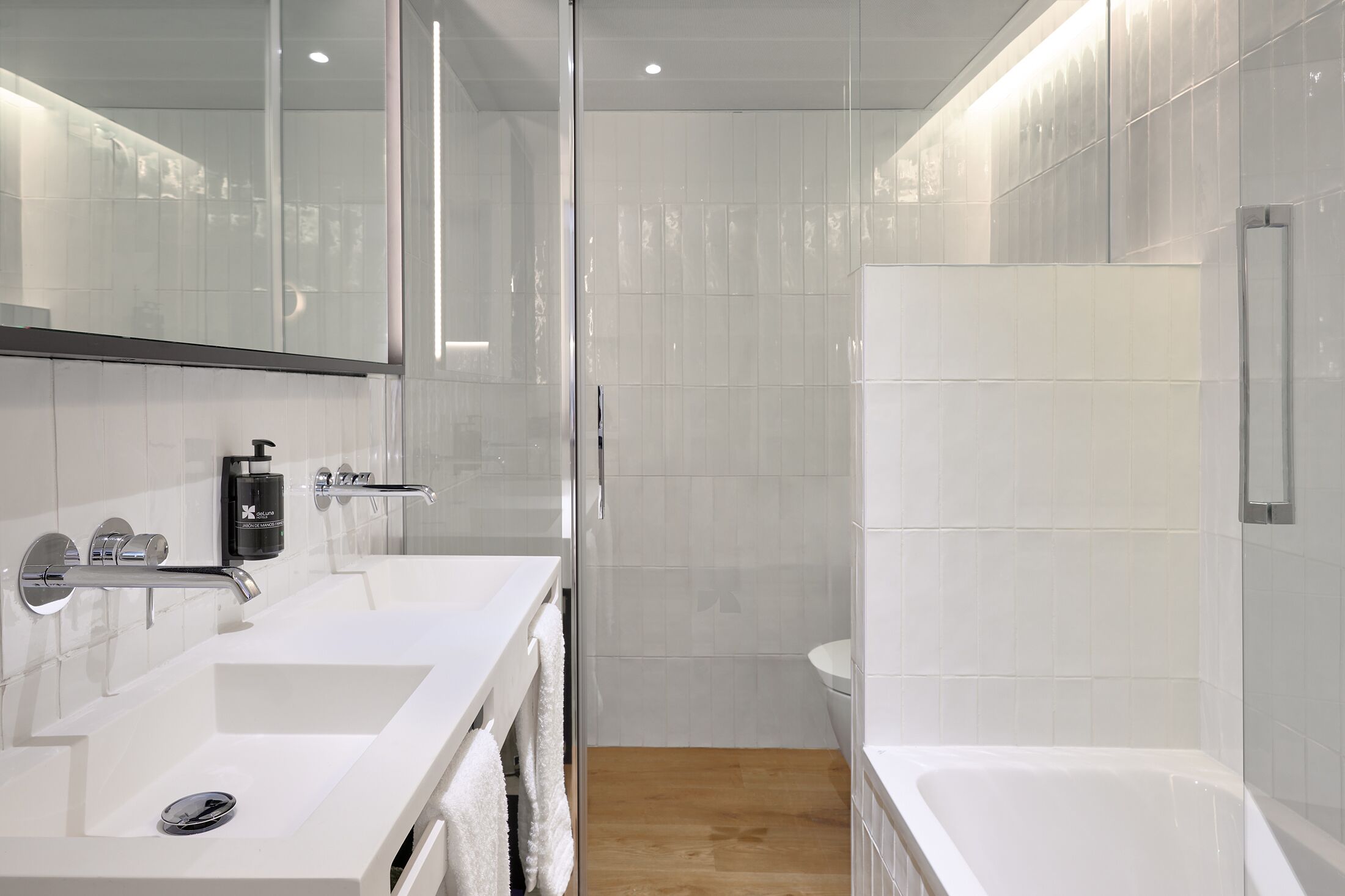 A modern bathroom with a glass shower enclosure, a white sink with a soap dispenser, and a bathtub.