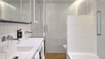 A modern bathroom with a glass shower enclosure, a white sink with a soap dispenser, and a bathtub.