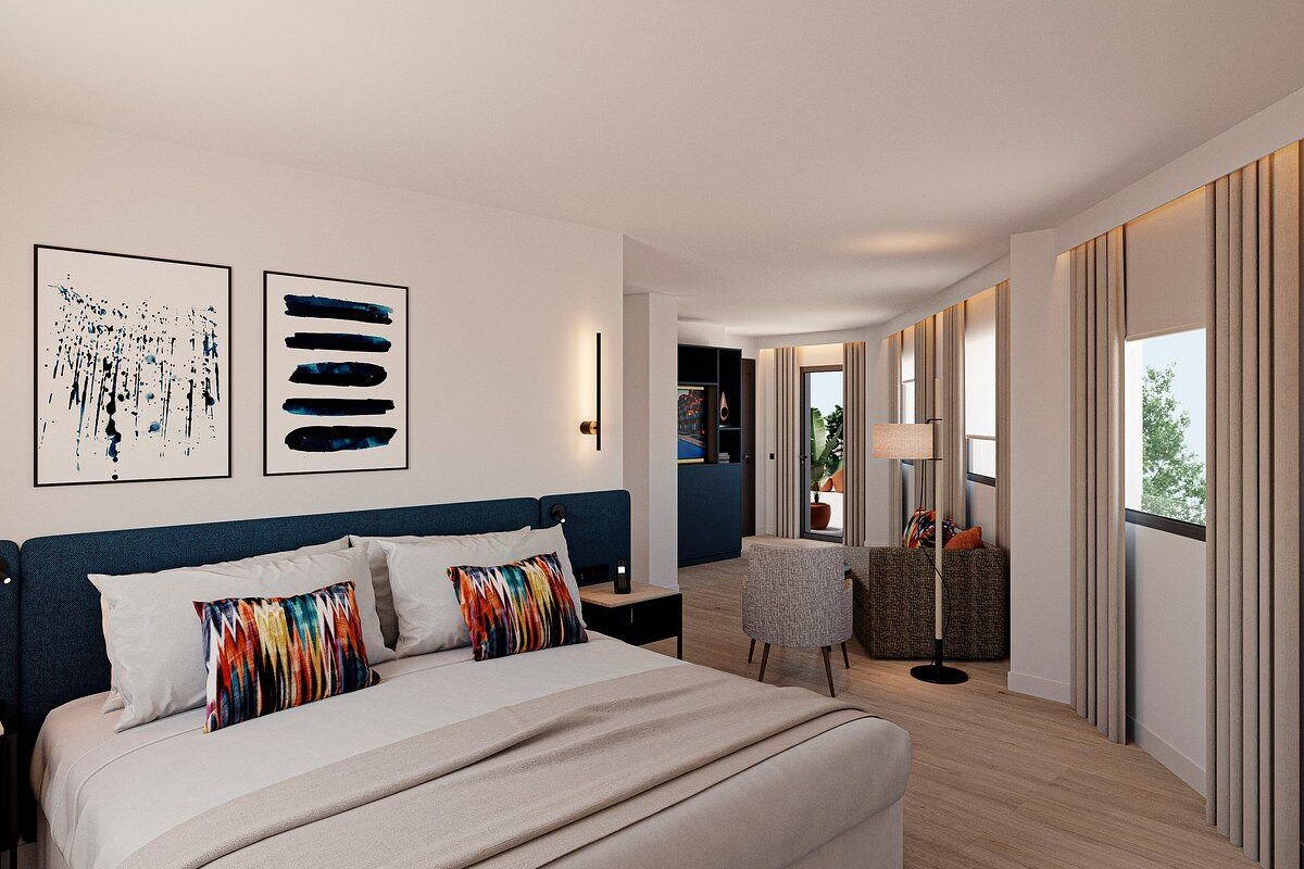 A modern hotel room with a large bed, a desk, a chair, and artwork on the walls.