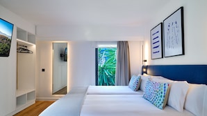 A modern hotel room with a large bed, a TV, a wardrobe, and a view of greenery through the window. - Apartamentos Luna Suites Granada (Granada)