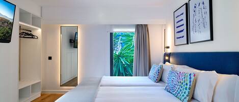 Ett modernt hotellrum med en stor säng, en TV, en garderob och utsikt över grönområden genom fönstret.