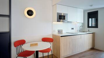Une cuisine moderne avec un plan de travail blanc, un four à micro-ondes encastré et un évier. On y trouve une table ronde avec deux chaises rouges et une petite plaque nominative.