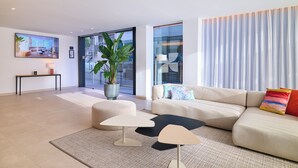 A modern living room with a sectional sofa, a coffee table, a side table, a potted plant, and a large window with curtains. - Apartamentos Luna Suites Granada (Granada)