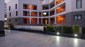 A multi-story hotel with a modern design, featuring balconies with wooden railings, a spacious outdoor area with benches, and a well-lit entrance. - Apartamentos Luna Suites Granada (Granada)
