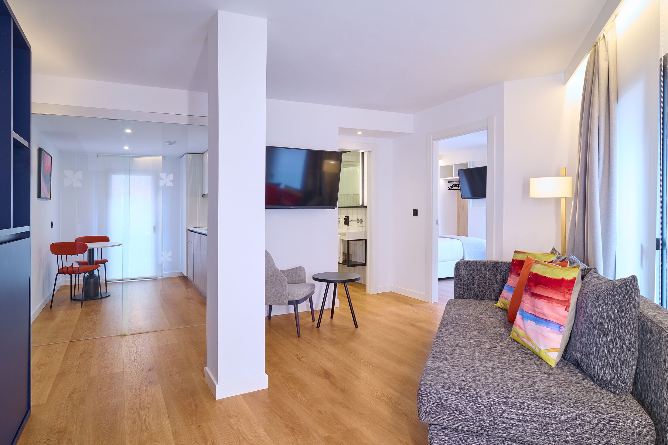 Una sala de estar moderna con un sofá gris, una mesita redonda y un televisor montado en la pared.