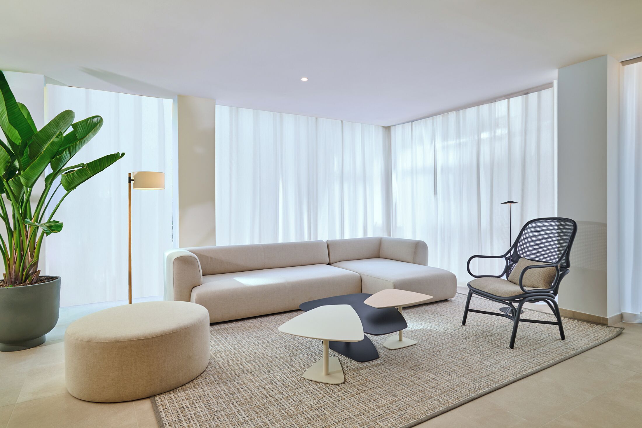 A modern living room with a beige sectional sofa, a round ottoman, a black mesh chair, and a small coffee table.