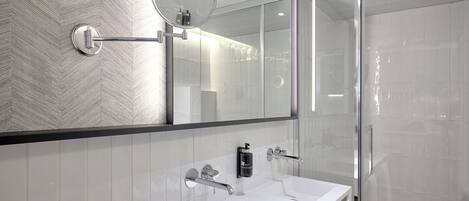 A modern bathroom with a large mirror, two sinks, and a glass shower enclosure.