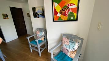A hallway with two grey chairs with blue cushions, a colorful abstract painting on the wall, and a door at the end.