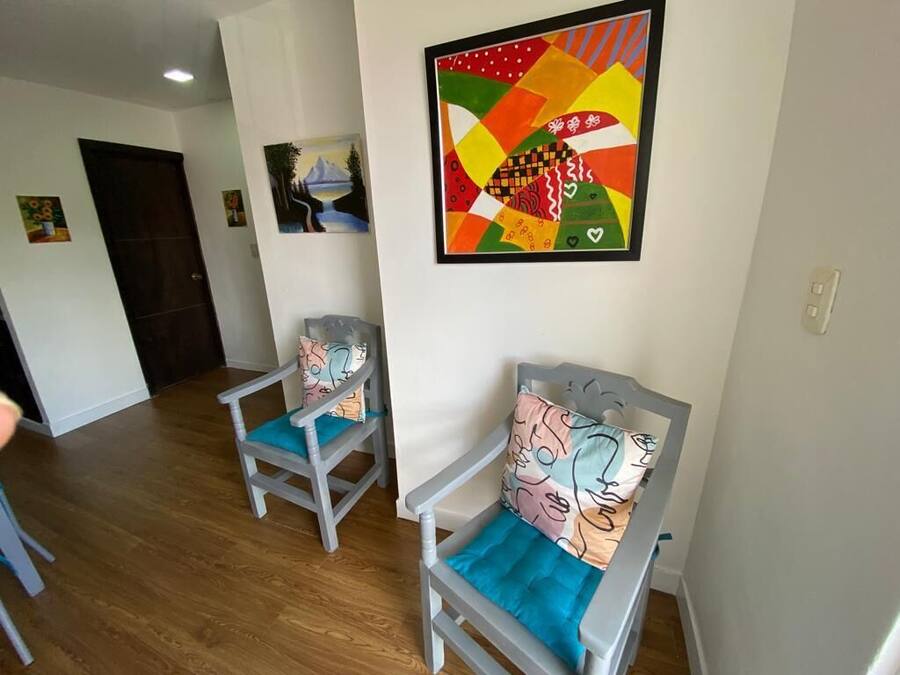A hallway with two grey chairs with blue cushions, a colorful abstract painting on the wall, and a door at the end.