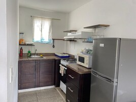 A compact kitchen with dark wooden cabinets, a stainless steel refrigerator, a microwave, and a gas stove.