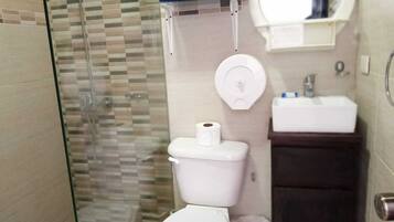 A bathroom with a glass shower enclosure, a toilet, a sink, and a towel rack with towels.