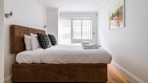 A bedroom with a large bed, white bedding, a brown headboard, and a window with a metal grille. - Gorgeous Kentish Town Flat (London)
