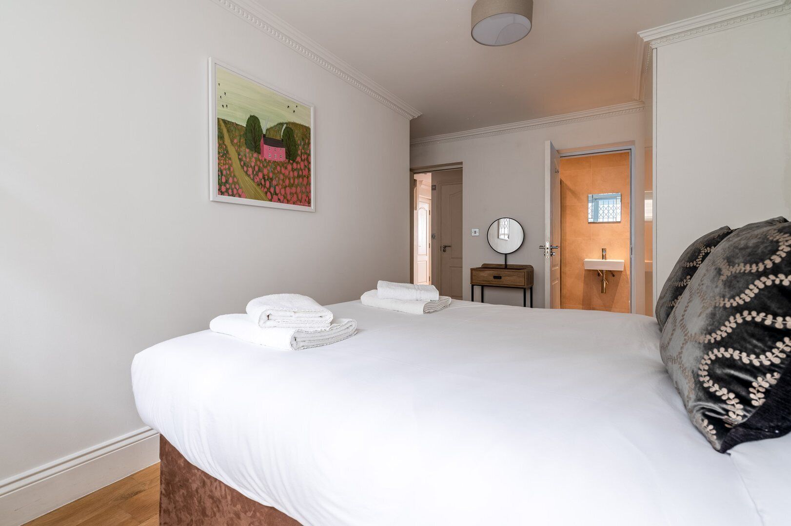 A hotel room with a large bed, a bedside table with a mirror, and a painting on the wall.
