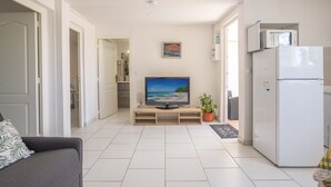Un salon moderne avec un téléviseur à écran plat, un réfrigérateur blanc et une plante en pot.