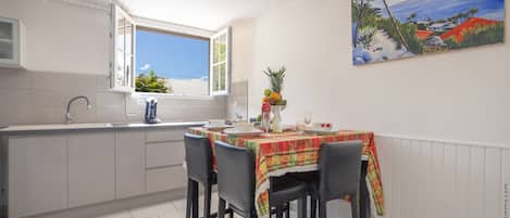 A kitchen with a dining area, a window with a view, and a painting on the wall.