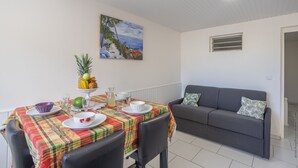 Un coin repas avec une table dressée pour deux personnes, un canapé gris et un tableau accroché au mur.