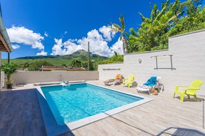 A rectangular swimming pool with a wooden deck, surrounded by bright yellow lounge chairs and a white wall. - Heliconia - Appt avec piscine partagée (Arrondissement of Saint-Pierre)