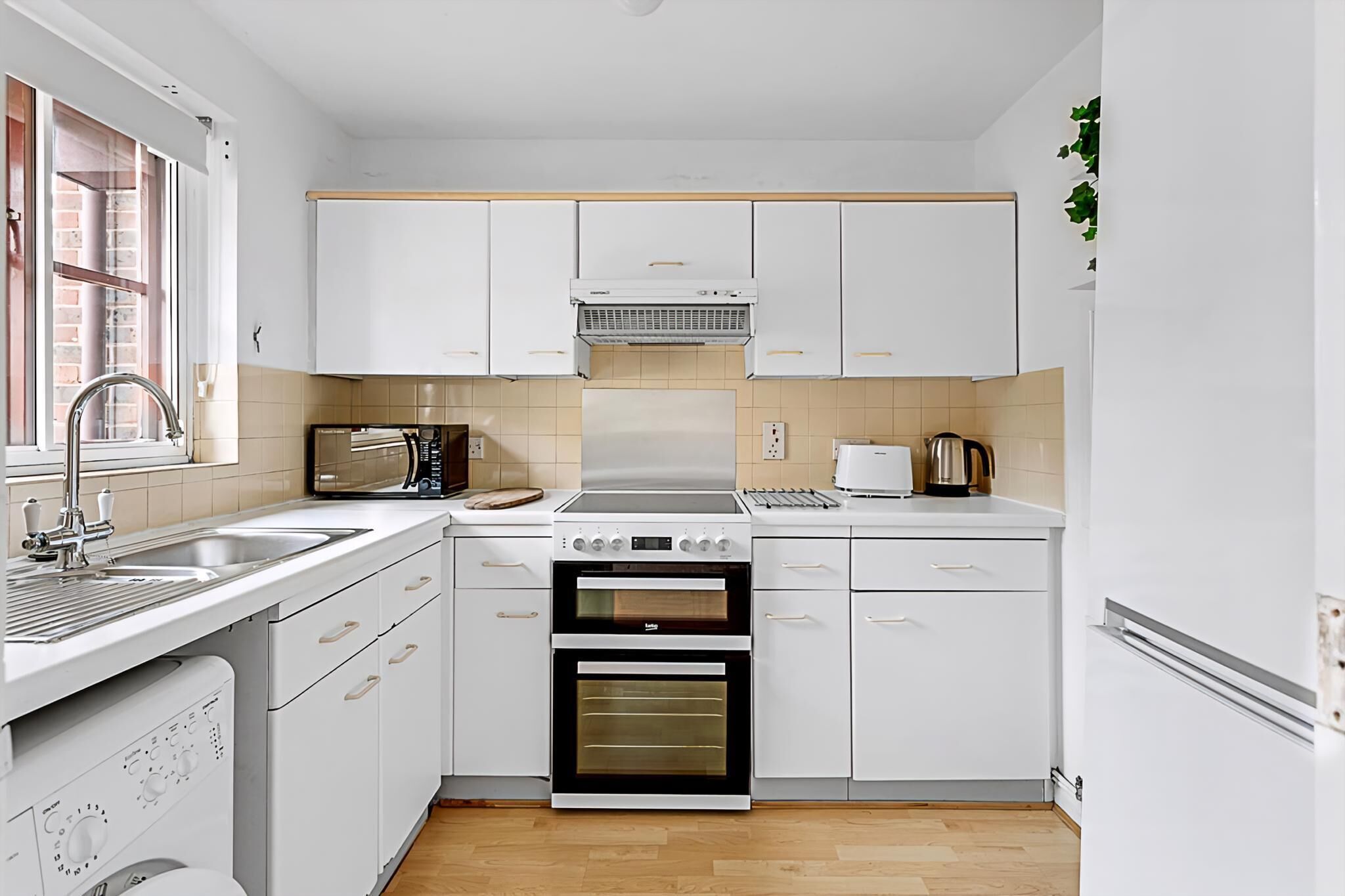 Una cocina moderna con armarios blancos, horno empotrado, microondas y pileta.