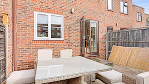 A patio with a glass-top table and wicker furniture against a brick wall. - Beautiful Three-bedroom House in Richmond (Richmond)