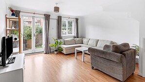 A modern living room with a sofa, a coffee table, and a TV. There is a sliding glass door leading to a garden. - Beautiful Three-bedroom House in Richmond (Richmond)