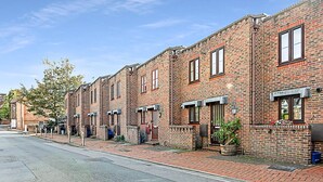 A row of brick townhouses with uniform windows and doors, a paved sidewalk, and a clear sky. - Beautiful Three-bedroom House in Richmond (Richmond)