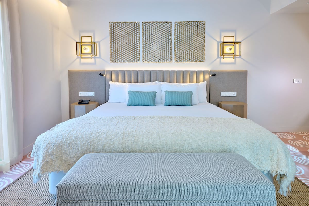 A hotel room with a large bed, two bedside tables, a bench, and decorative wall panels.