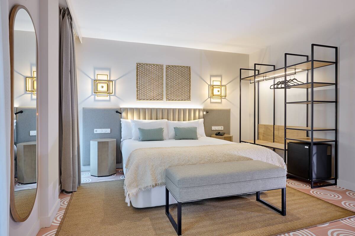 A modern hotel room with a large bed, bedside tables, a wardrobe, and a mirror.