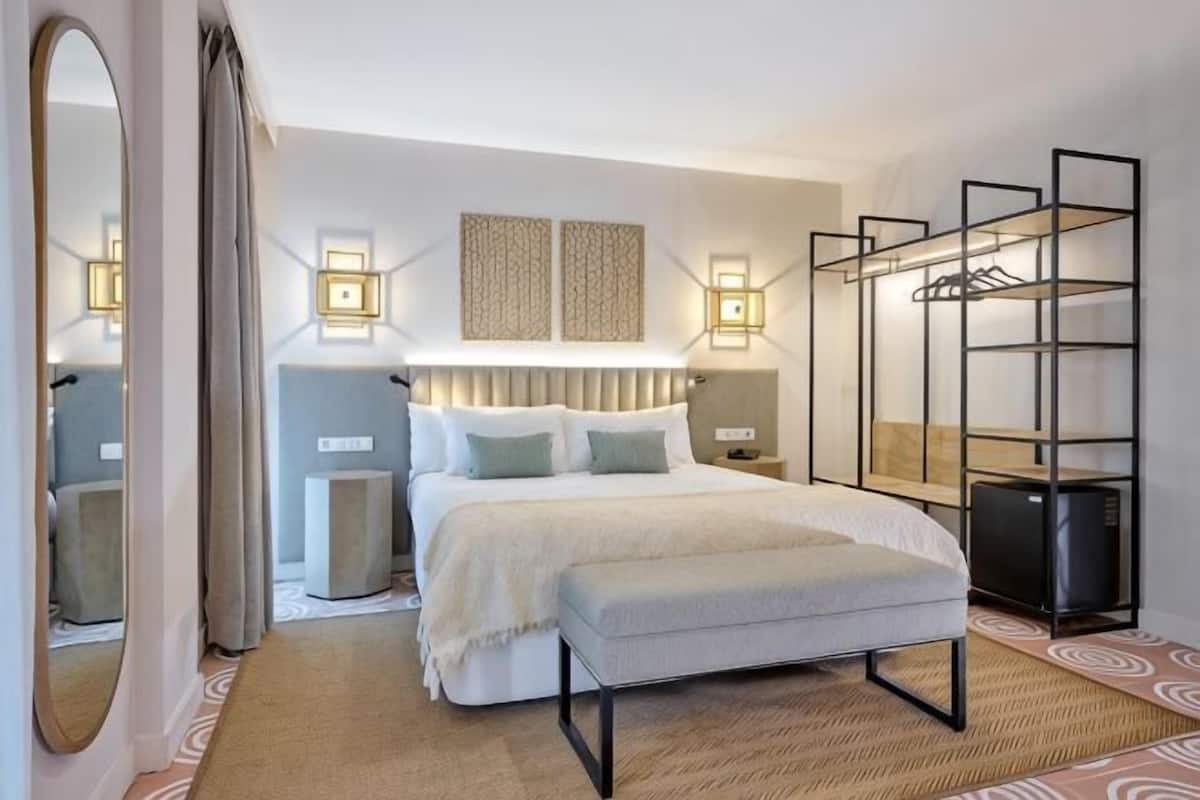 A bedroom with a bed, bedside tables, a mirror, a wardrobe, and wall-mounted lighting.