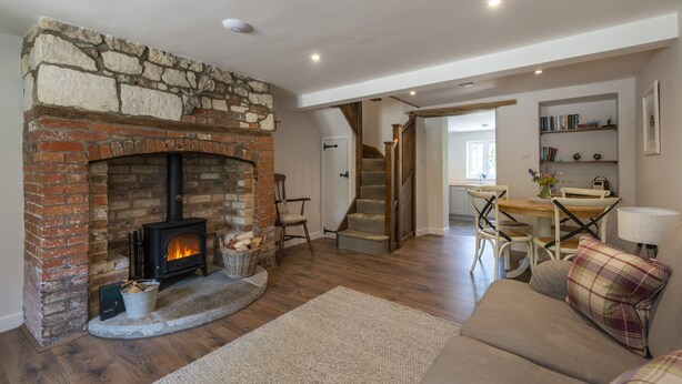 A cozy living room with a stone fireplace, wooden flooring, a sofa, and a staircase leading to another room. - Cosy cottage in a pretty village with a pub at the end of the garden! (Buckland Newton)