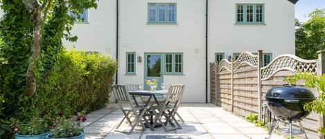 Une maison à deux étages dotée d’un patio comprenant une table et des chaises, un barbecue et des plantes en pot.