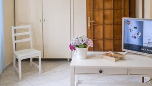 A room with a white desk, a white chair, a wooden door, and a television on the desk. - La Natura x9 (Sorrento)