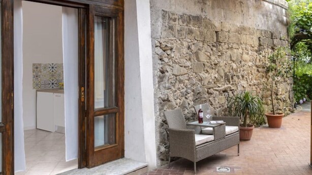 A stone wall with a wicker sofa and potted plants. - La Natura x9 (Sorrento)