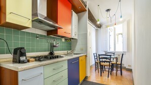 Una cocina con estufa a gas, cafetera y pileta. Hay un comedor con mesa y sillas.