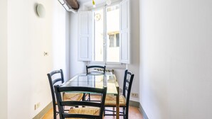 Un comedor con una mesa de vidrio, cuatro sillas y una ventana con persianas blancas.